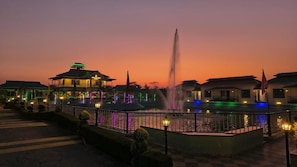 Hotel amb una font d'aigua, il·luminat per llums de colors i un edifici tradicional amb teulada verda.