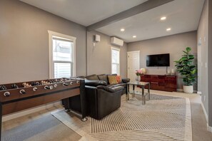 A living room with a foosball table, a leather sofa, a coffee table, and a television mounted on the wall. - 4B2B DT Everett Ideal for Medical/Corporate/Insurance Placement close Hospital (Everett)