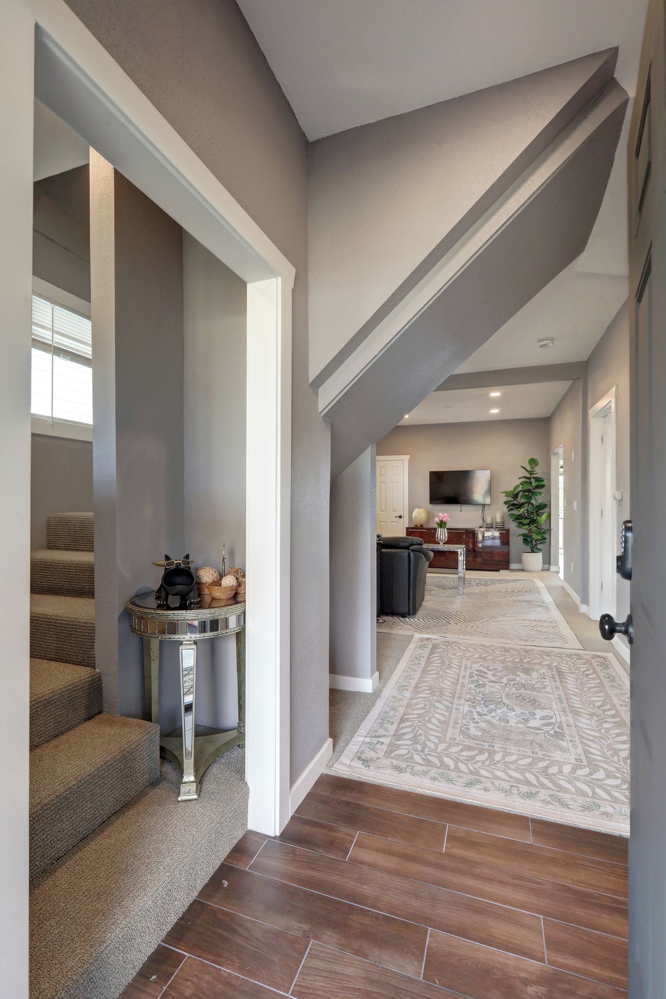 A hallway with a staircase, a console table with decorative items, a television, and a potted plant.