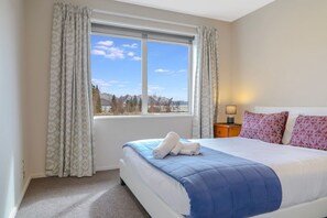 Ein Hotelzimmer mit einem großen Bett, einem Fenster mit Blick auf Bäume und Berge sowie einem Nachttisch mit einer Lampe.