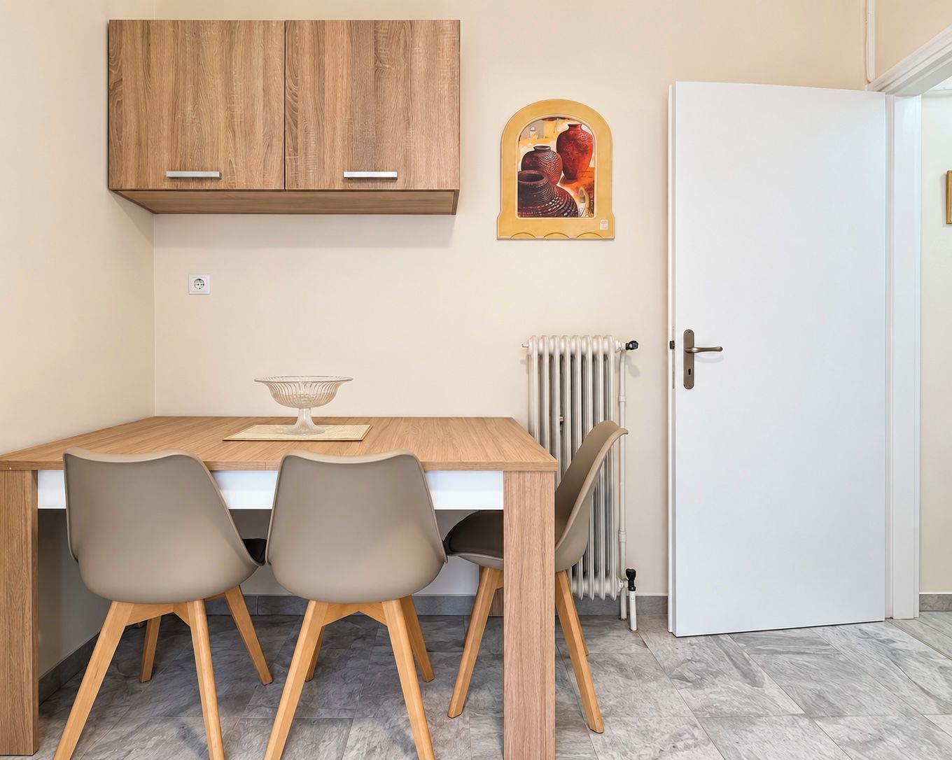 A dining area with a wooden table, two chairs, a white radiator, and a white door.
