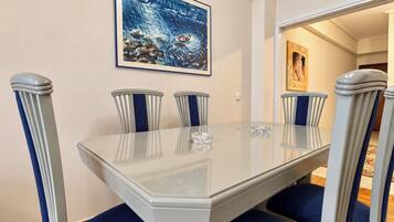 A dining area with a glass table, blue upholstered chairs, and a framed artwork on the wall.