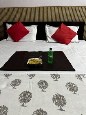 Cama bem arrumada com um edredom preto, duas almofadas vermelhas, uma garrafa de Sprite e uma bandeja com comida.