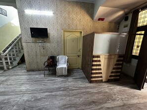 Une pièce avec un sol en marbre, un meuble en bois, une chaise avec un sac, un téléviseur fixé au mur et un escalier.