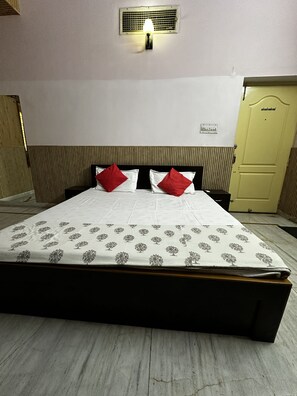 Une chambre d’hôtel comprenant un lit, une table de chevet, une lampe fixée au mur, une porte et une prise électrique.