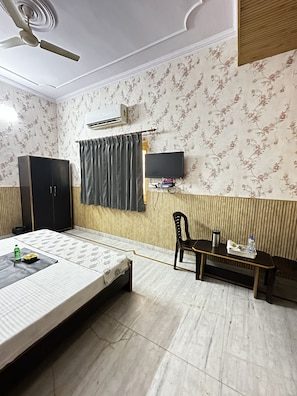 Quarto com cama, escrivaninha, cadeira, televisão e ar condicionado.