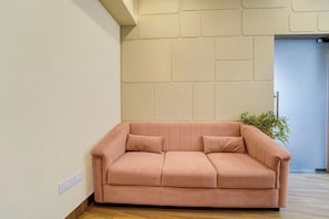 Una sala moderna con un sofá rosa, piso de madera y una pared con diseño geométrico.