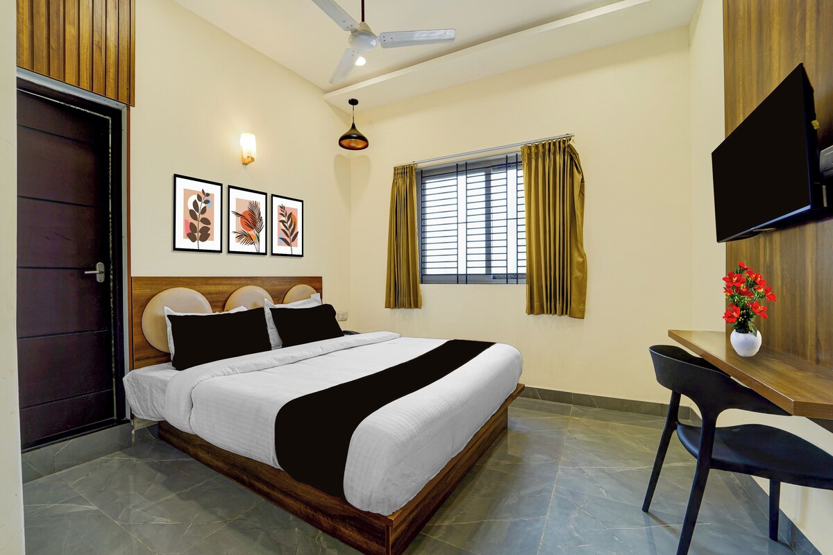 Habitación de hotel con cama, escritorio, televisión y ventana con cortinas.