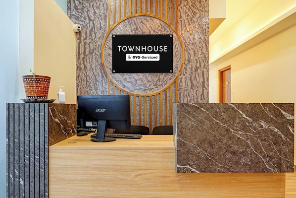 A reception desk with a monitor, keyboard, and a sign that reads 'TOWNHOUSE' and 'OYO-Serviced'.