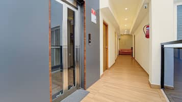 A hallway with a wooden floor, a glass elevator door, and a fire extinguisher mounted on the wall.