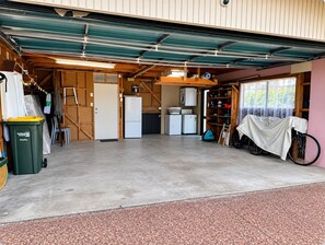 Een garage met een betonnen vloer, een fiets, een wasmachine en een koelkast.