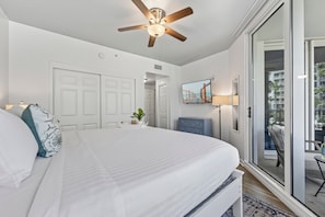 A hotel room with a large bed, a ceiling fan, a TV, and a view of the ocean through the sliding glass door. - Poolside Paradise Resort Pool (Destin)