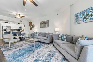 A modern living room with a sofa, chairs, a coffee table, and a dining area with a kitchen in the background. - Poolside Paradise Resort Pool (Destin)