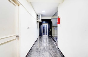 Un pasillo con piso de mármol, una puerta a la izquierda y un extintor a la derecha.