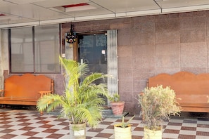 Un área de recepción con piso a cuadros, dos bancos de madera y plantas en macetas.