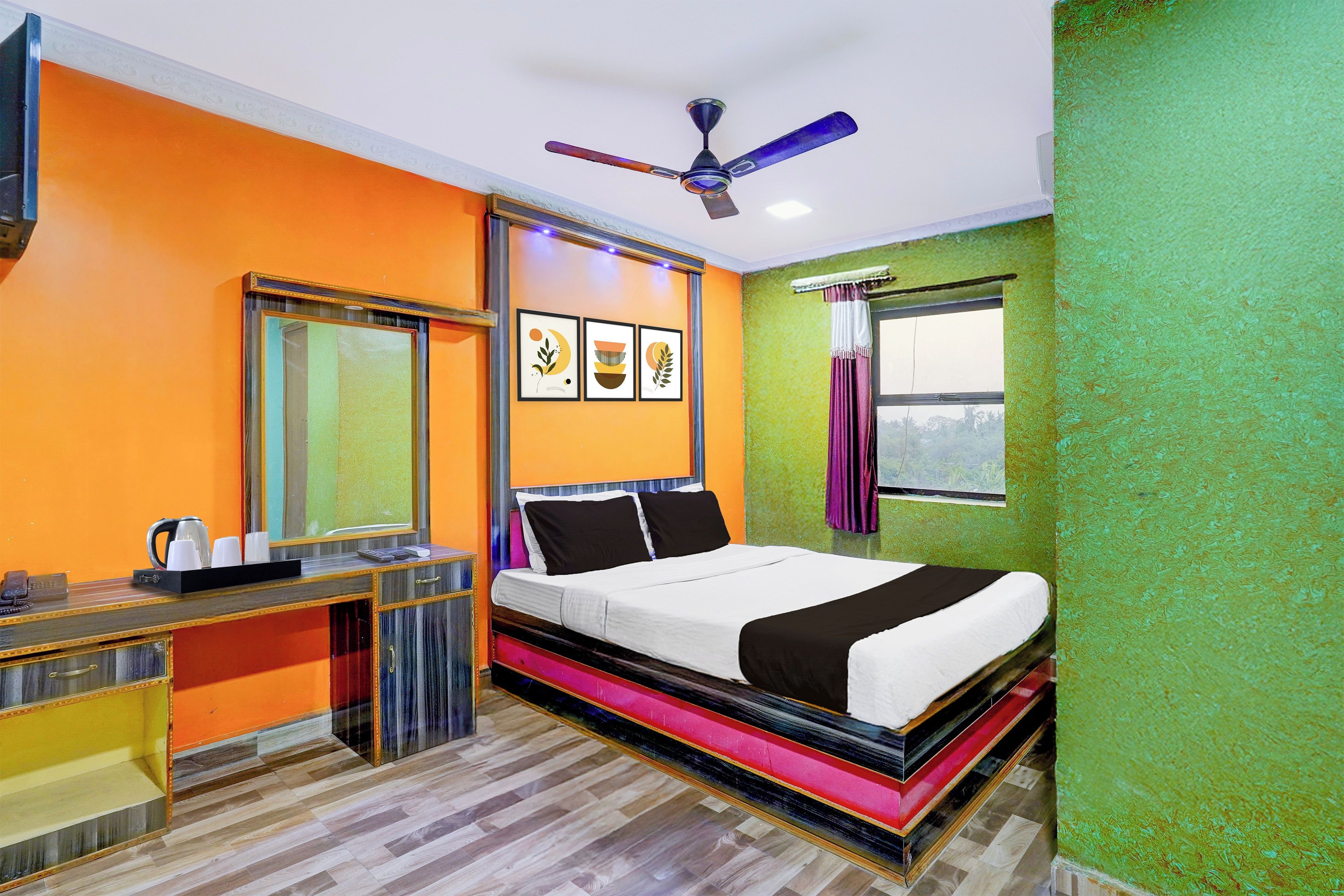A hotel room with a bed, a desk, a telephone, a ceiling fan, and framed artwork on the wall.