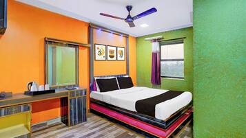 A hotel room with a bed, a desk, a telephone, a ceiling fan, and framed artwork on the wall.