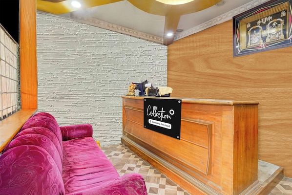 A reception area with a wooden reception desk, a plush pink sofa, and a patterned tiled floor.
