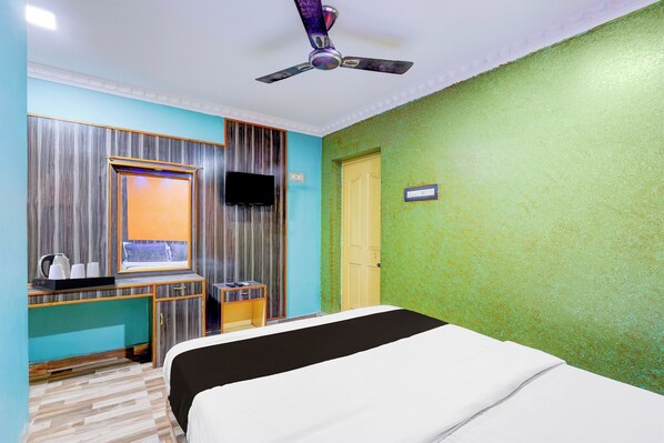 A hotel room with a bed, a desk with a mirror, a television, and a ceiling fan.