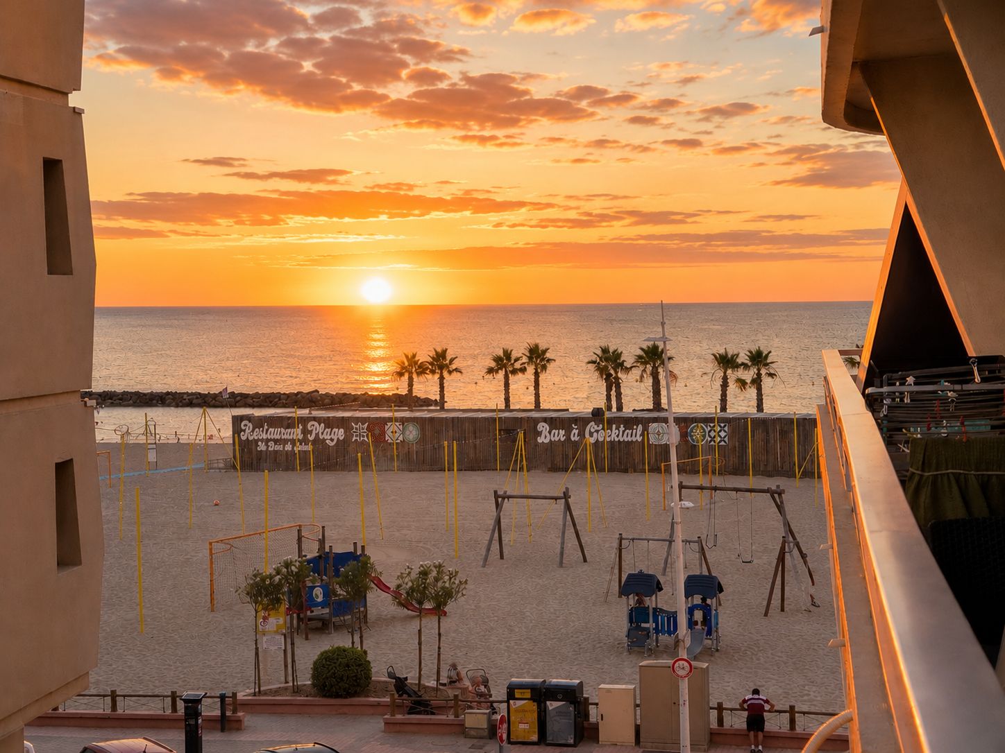 A beach view with a sunset, palm trees, a playground, and a bar.