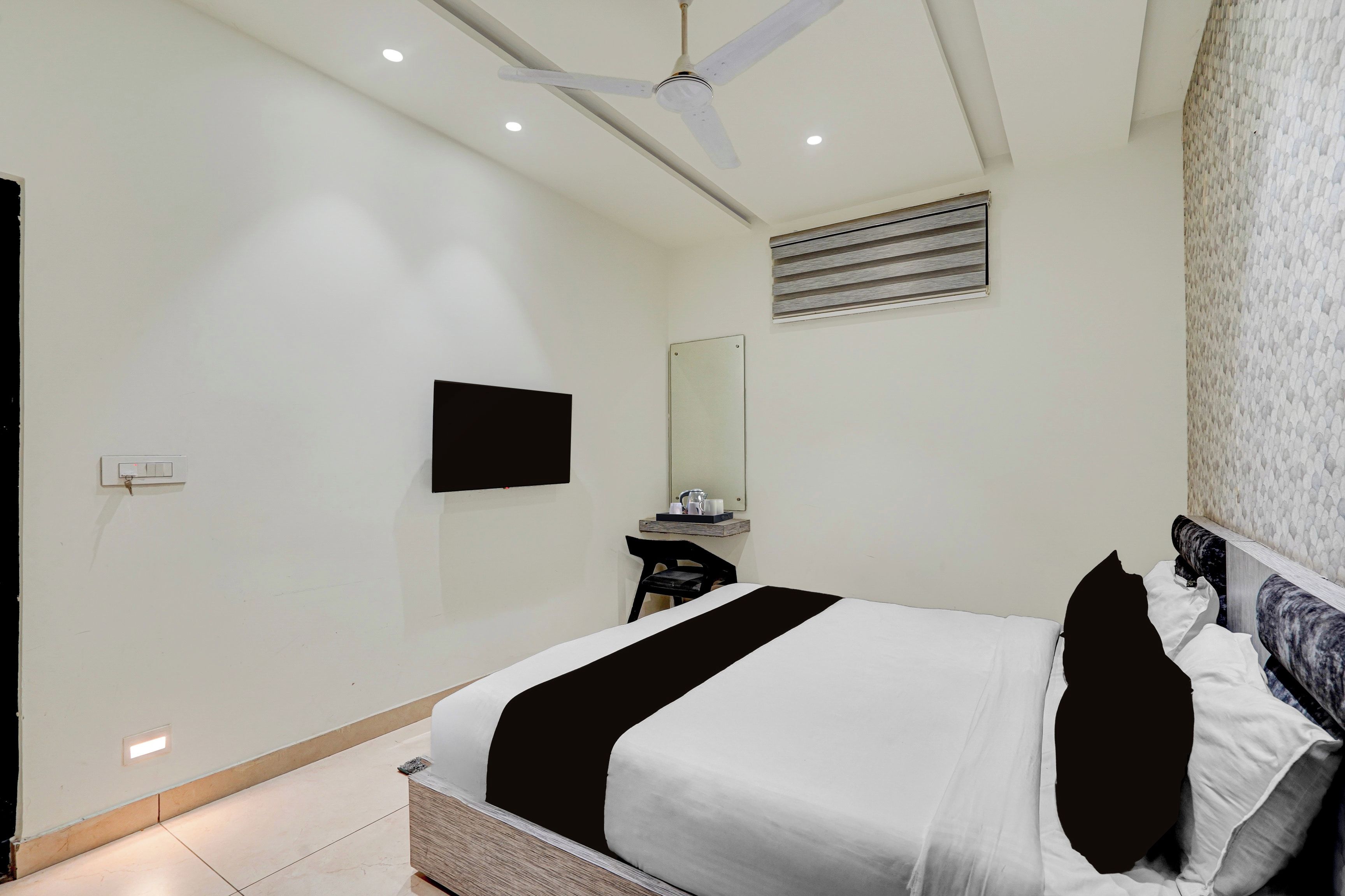 Habitación de hotel con cama, un televisor de pantalla plana en la pared, ventilador de techo y ventana con persianas.