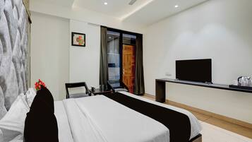 A hotel room with a bed, a desk with a flat-screen TV, a chair, and a window with curtains.