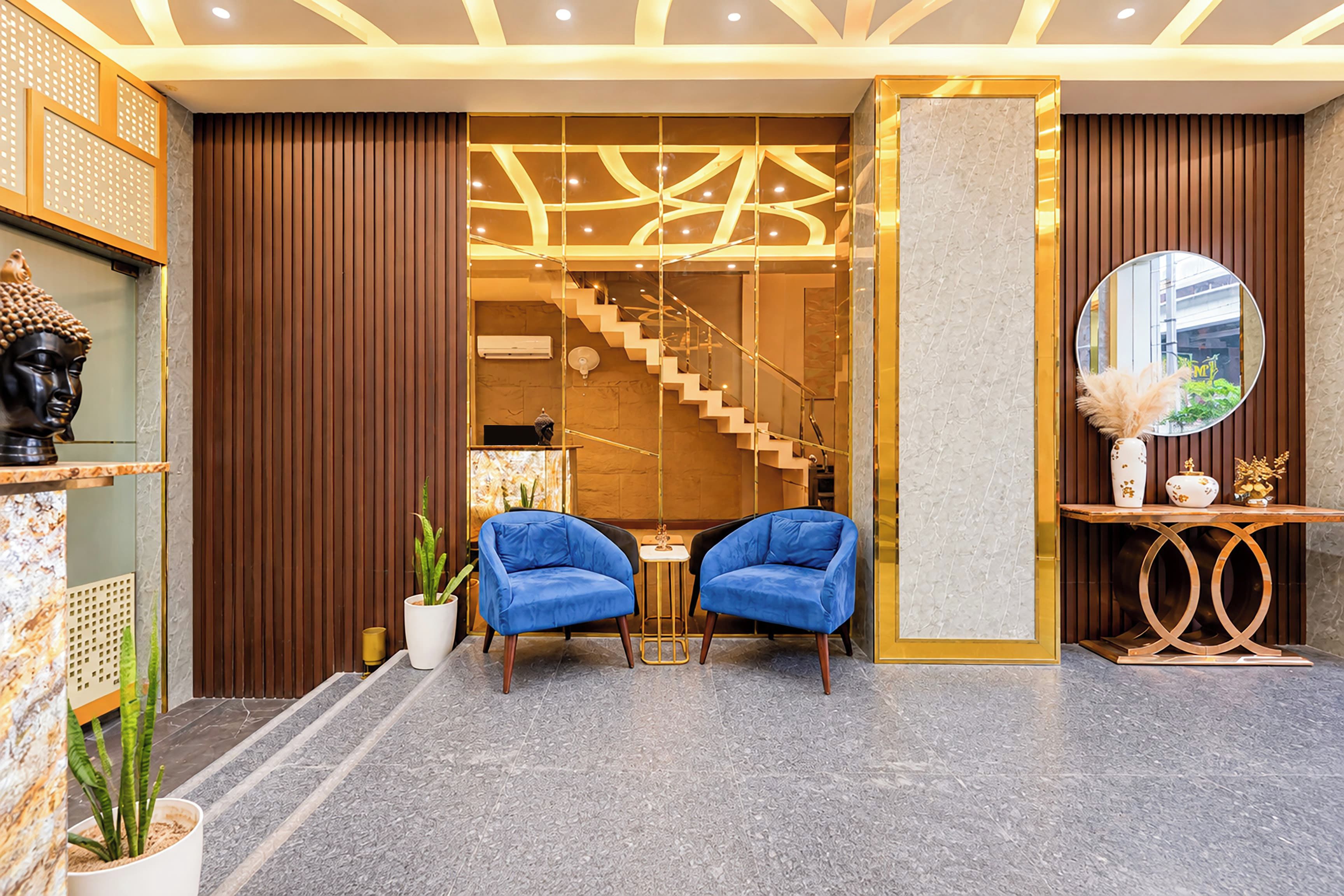 A modern lobby with a staircase, two blue chairs, and a decorative Buddha statue.