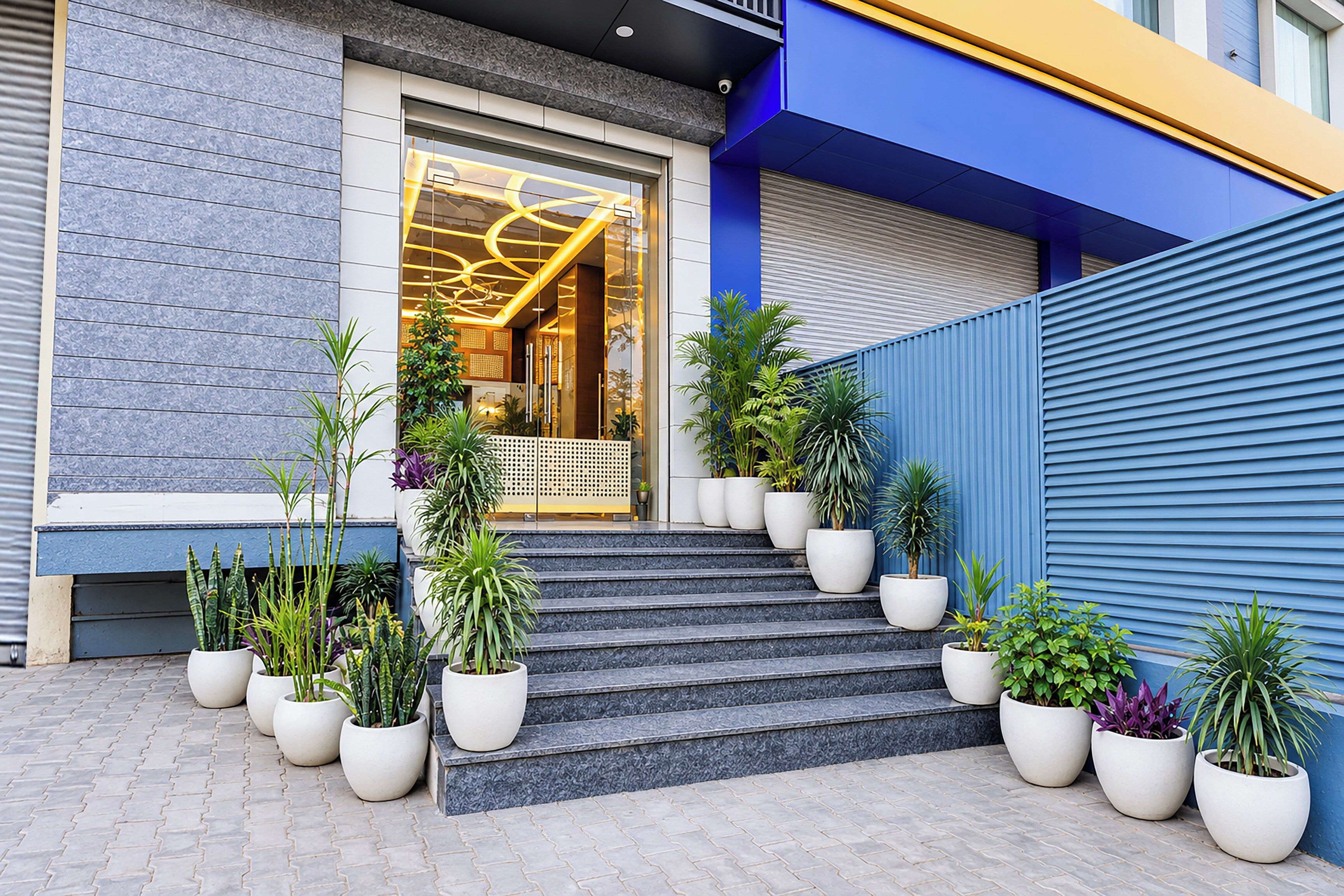 A building entrance with a glass door, steps leading up to it, and potted plants arranged in front.