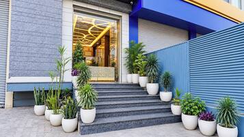 A building entrance with a glass door, steps leading up to it, and potted plants arranged in front.