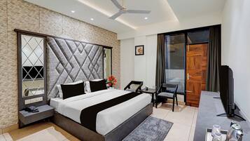 A modern hotel room with a large bed, a desk, a chair, a TV, and a ceiling fan.