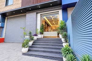 A building entrance with a set of steps leading up to a glass door, flanked by potted plants and a closed garage door.