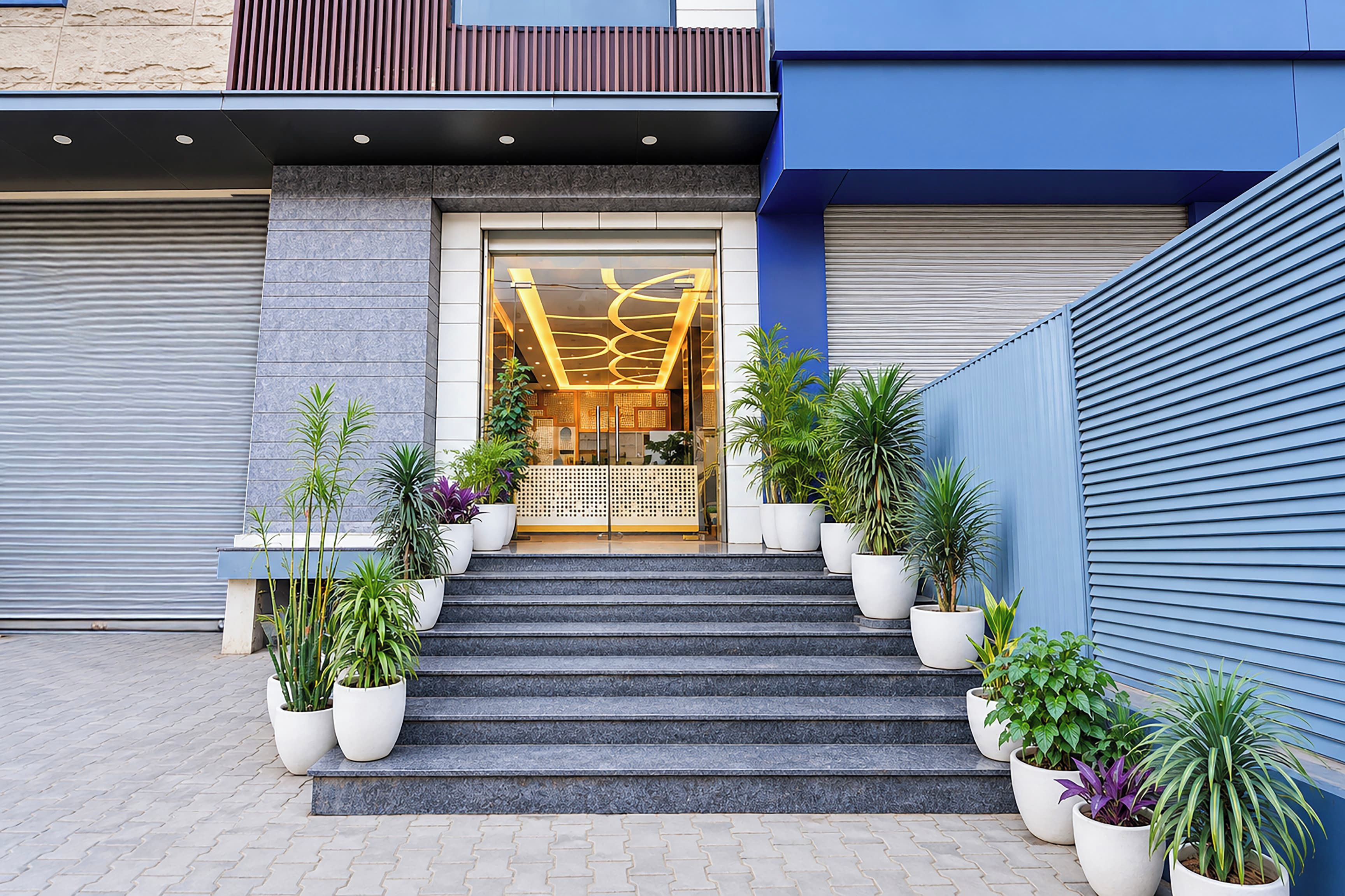 A hotel entrance with a set of stairs leading to a door with a modern design. There are potted plants on either side of the stairs.