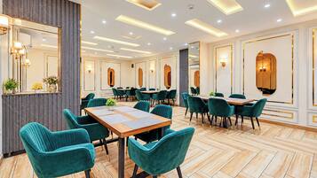 A modern hotel dining area with wooden tables, teal chairs, and a herringbone floor pattern.
