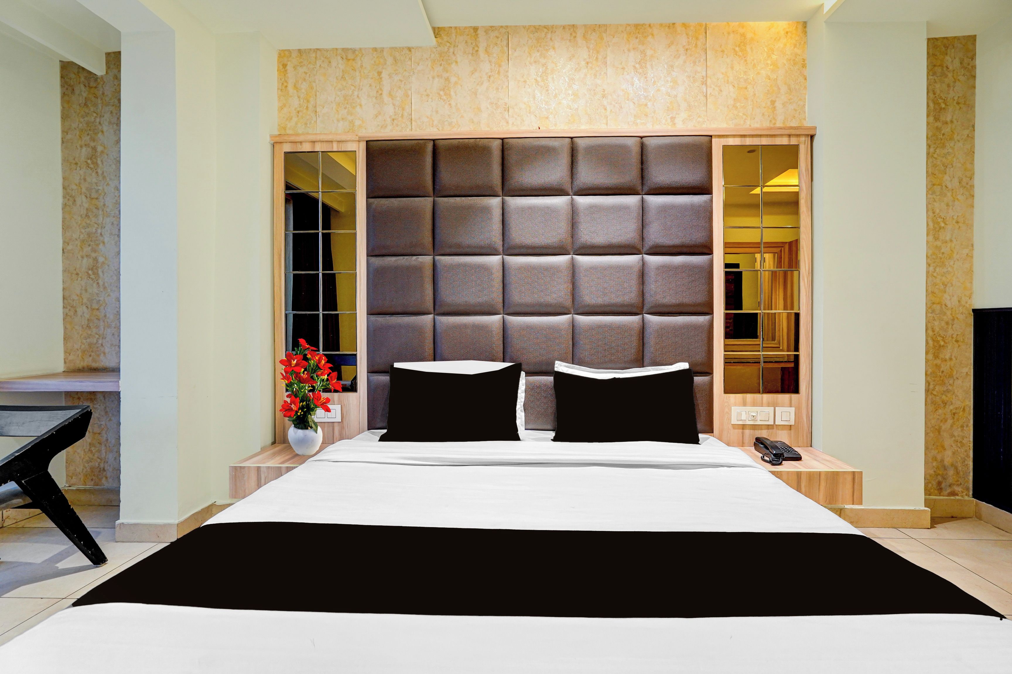 Quarto moderno com cama grande, cabeceira estofada, mesa de cabeceira com telefone e vaso com flores.