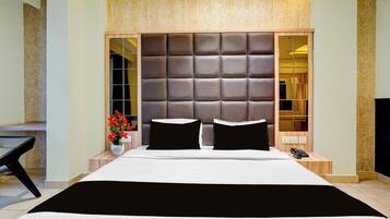 Quarto moderno com cama grande, cabeceira estofada, mesa de cabeceira com telefone e vaso com flores.
