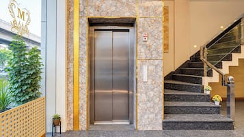 Un ascensor con pared de mármol y una escalera con barandilla de cristal.