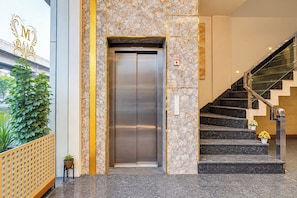 An elevator with a marble wall and a staircase with a glass railing. - Super Townhouse Oak Ambala Formerly (Ambala)