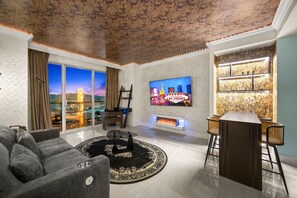 A modern living room with a large TV, a fireplace, a bar area, and a view of the cityscape through large windows. - Palace in the Sky|Vegas Strip Balcony/Sphere/Pools (Las Vegas)
