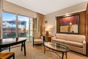 A hotel room with a sofa, armchair, glass coffee table, and a view of the city through large windows. - Vegas Sky Suite | Extended Balcony + Strip Views (Las Vegas)