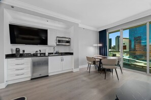 A modern kitchen with a flat-screen TV, microwave, and built-in oven. There is a dining area with a table and chairs, and a large window offering a view of the city. - Modern Vegas Escape|Private Balcony+Strip Views! (Las Vegas)