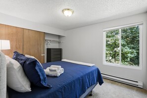 Un dormitorio con cama, armario, ventana con vista a árboles y una lámpara en el techo.