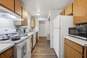 Una cuina moderna amb armaris de fusta, un refrigerador blanc, un microones i una estufa.