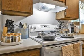 Una cocina con estufa blanca, un cartel que indica café y té, y diversos utensilios de cocina.