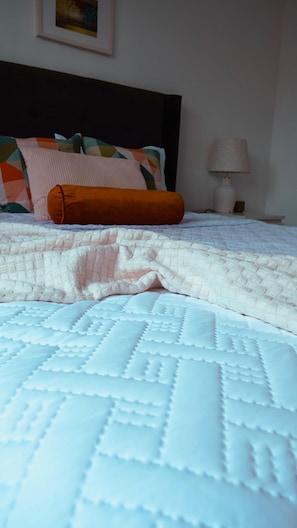 Een bed met een witte quilt en een opgevouwen oranje deken.