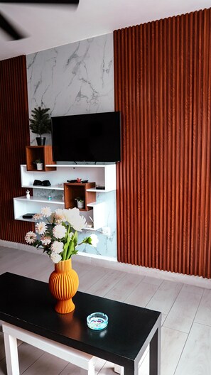 Een moderne woonkamer met een flatscreen televisie aan de wand, een houten tv-meubel eronder en een zwarte salontafel met een bloemenvaas.