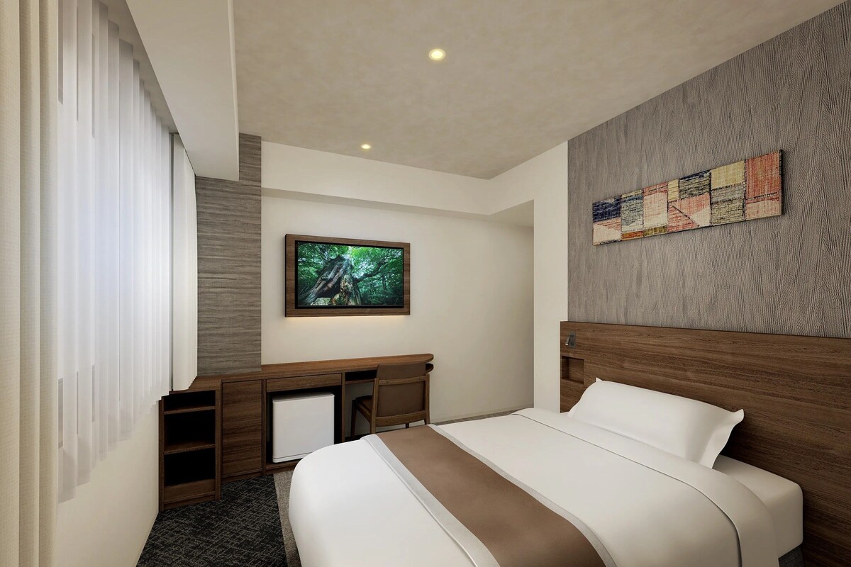 A hotel room with a bed, a desk, a television, and a wall-mounted artwork.