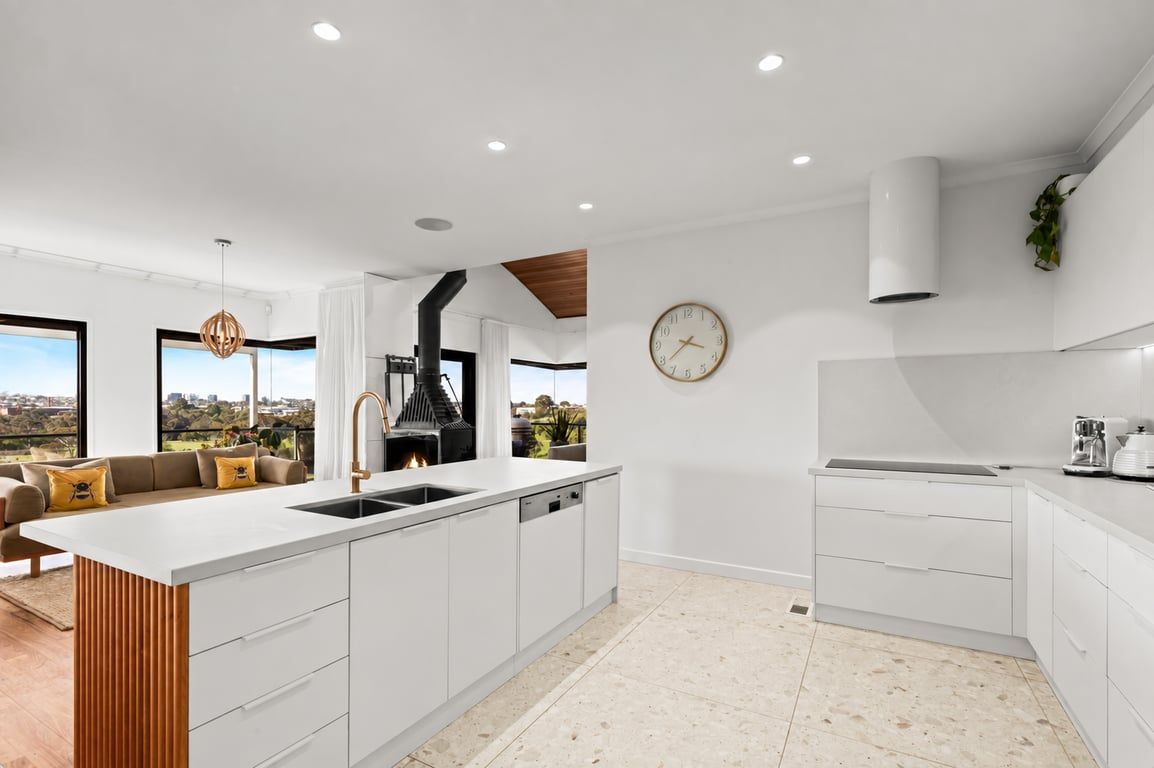 Une cuisine moderne dotée d’un îlot central, de meubles blancs et d’une grande fenêtre offrant une vue sur l’extérieur.