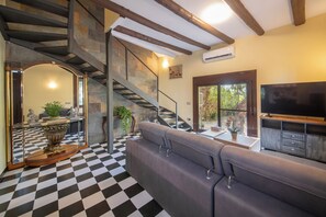 A living room with a checkered floor, a grey sofa, a staircase with stone walls, and a TV on a wooden stand. - Boutique Villa Marcia—Adults Only, 10 minutes from the beach. (Altafulla)