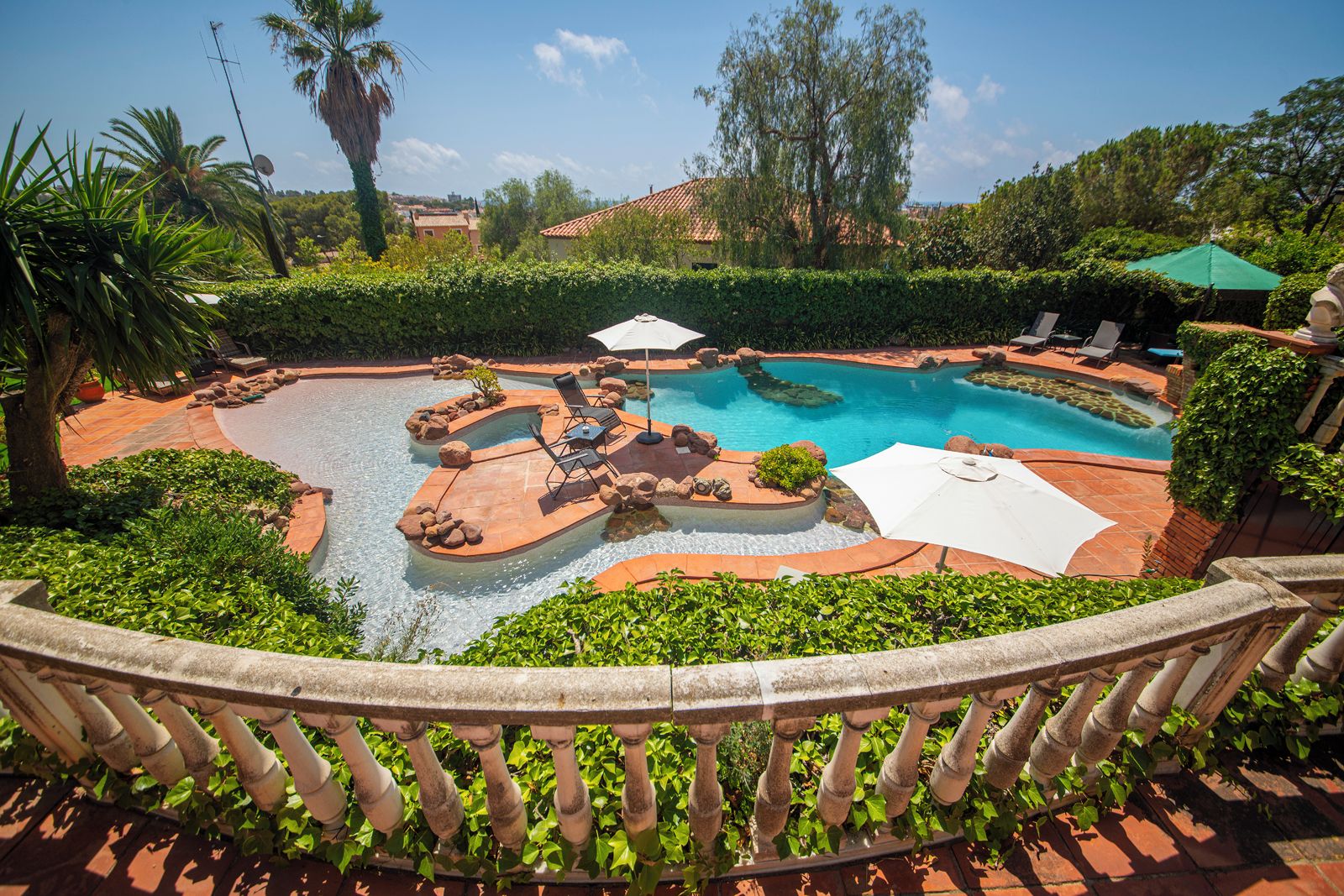 A pool area with a curved design, lounge chairs, and umbrellas.