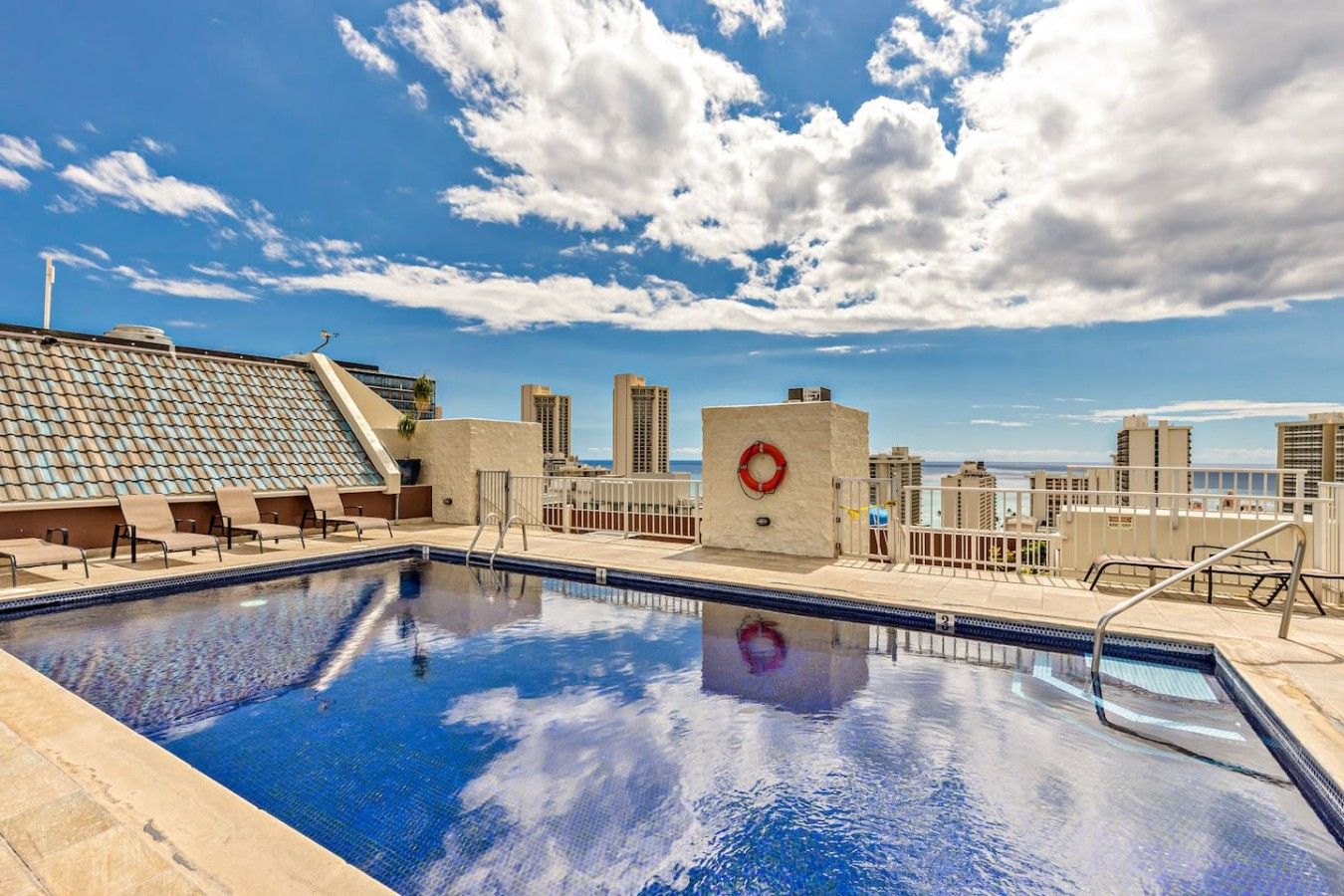 A rooftop pool with clear blue water, a lifebuoy, and a view of the city skyline.